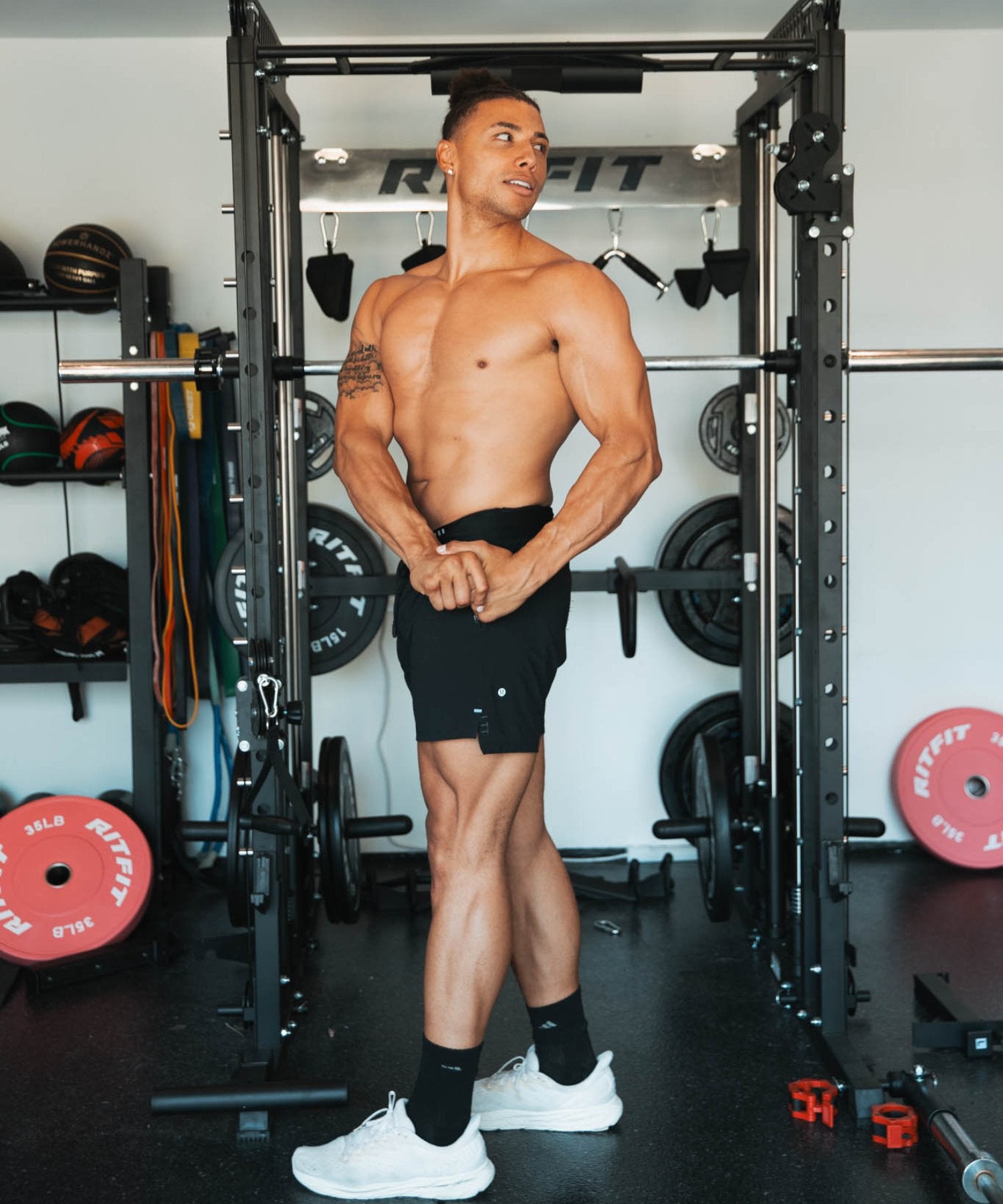 Chase DeMoor standing shirtless in home gym with black power rack and weights