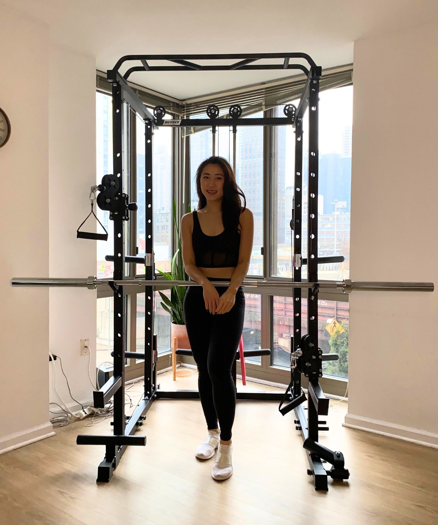 Woman standing in a bright homegym with a black power rack and barbell