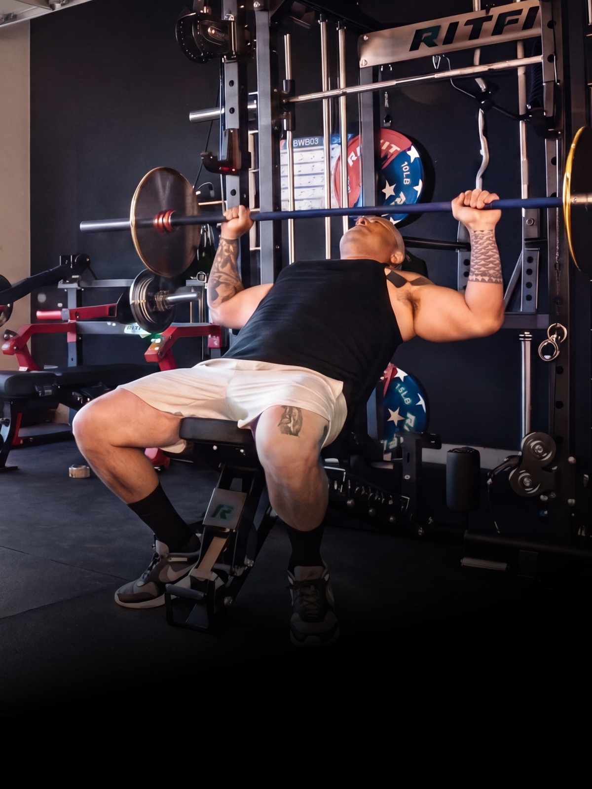 Tattooed man performing bench press on RitFit power rack with barbell