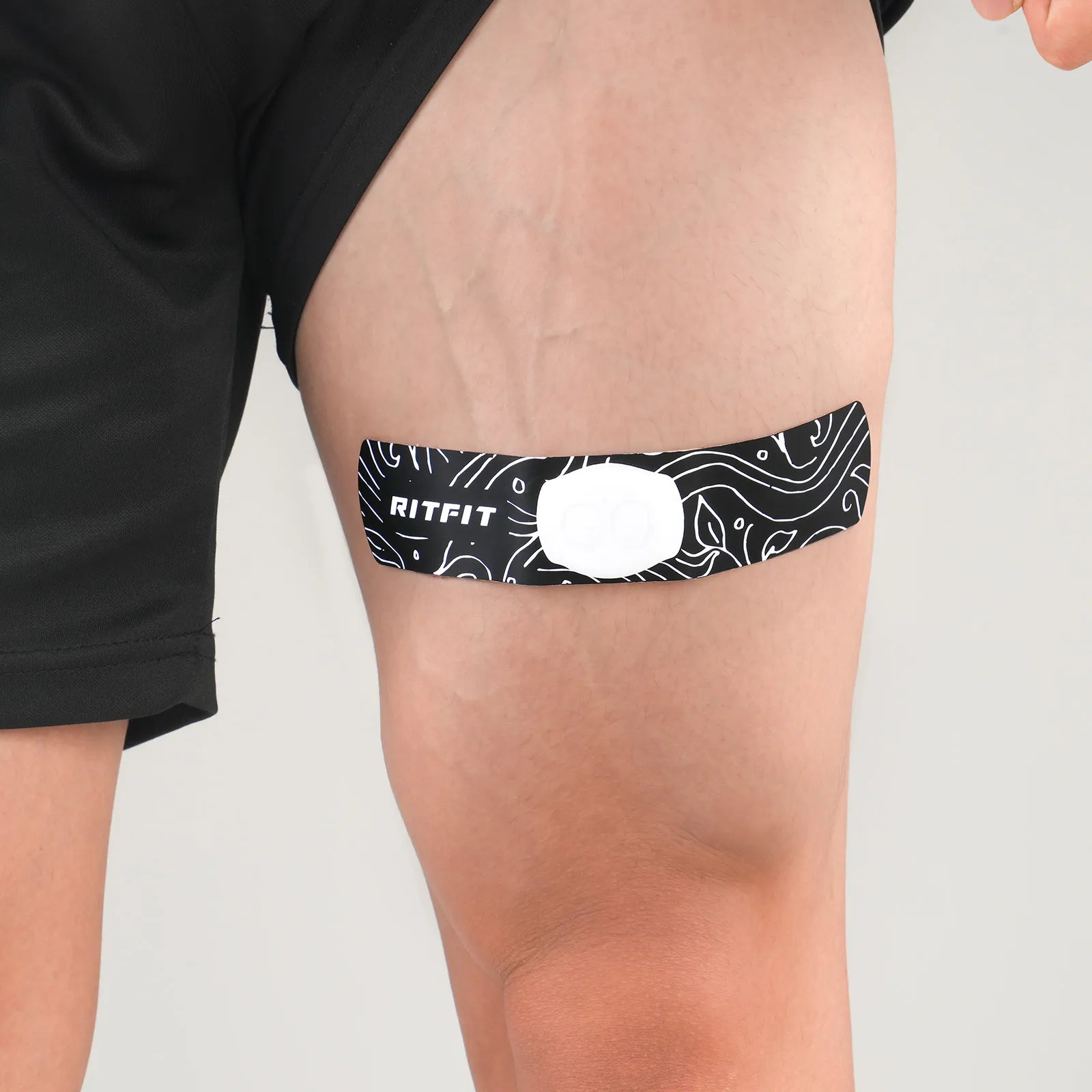 Black and white RitFit Wireless EMS Muscle Stimulator attached to a person's thigh