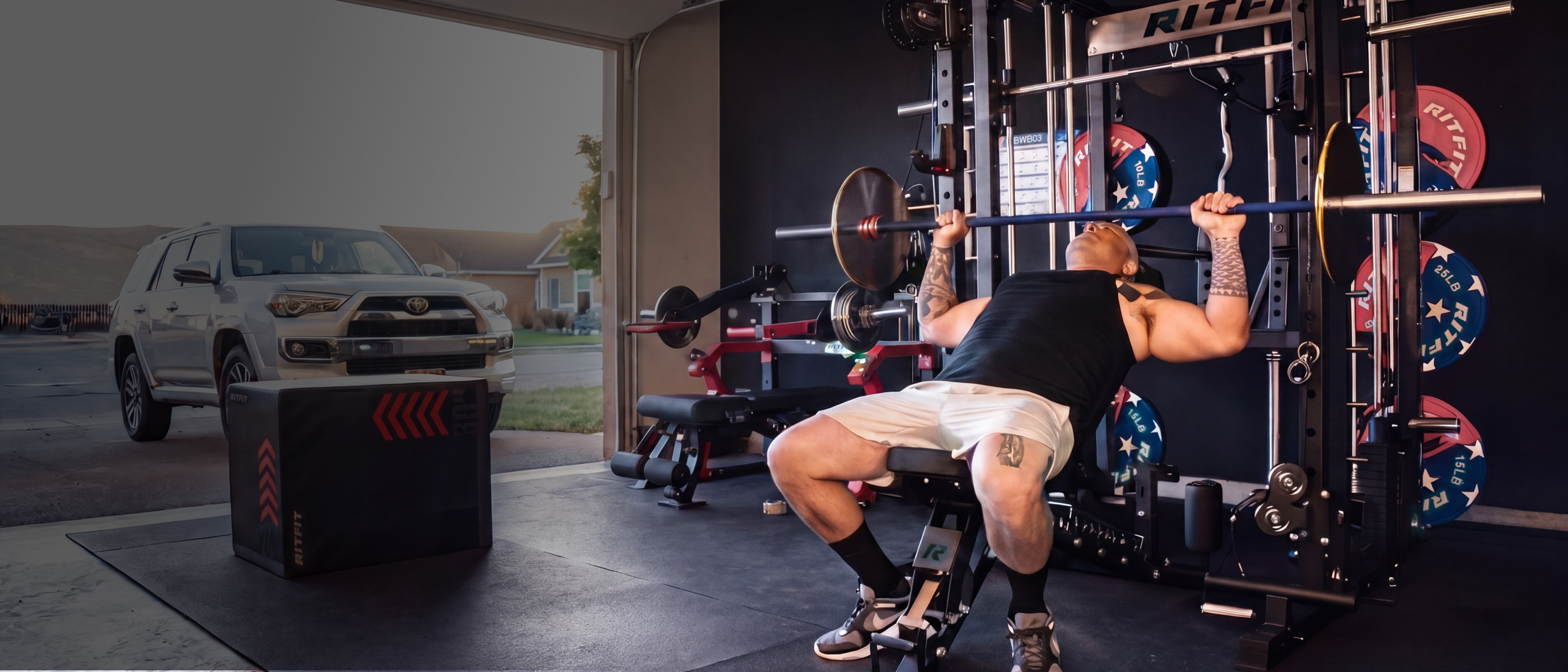 Man performing bench press on RitFit power rack in home garage gym with weight plates