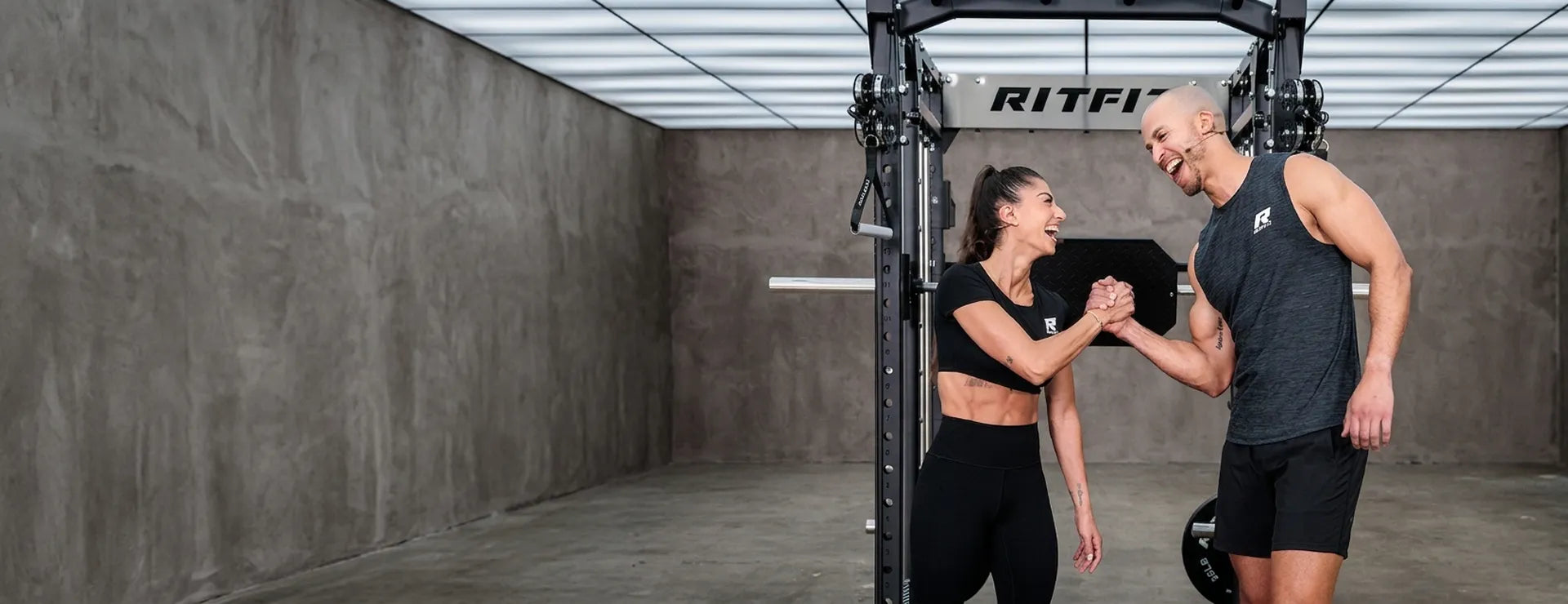 Smiling couple high-fiving near black Ritfit power rack in concrete gym