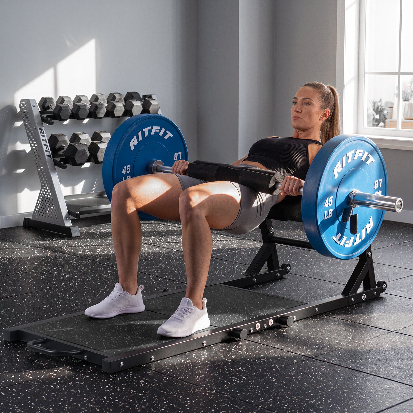 Woman performing hip thrusts on black RitFit PHM02 Hip Thrust Machine with blue weight plates